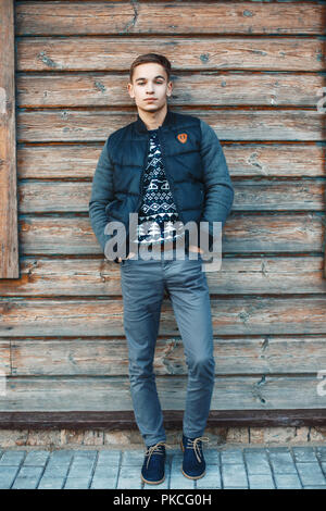 Stylish young man stands against a background of a wooden house. Stock Photo