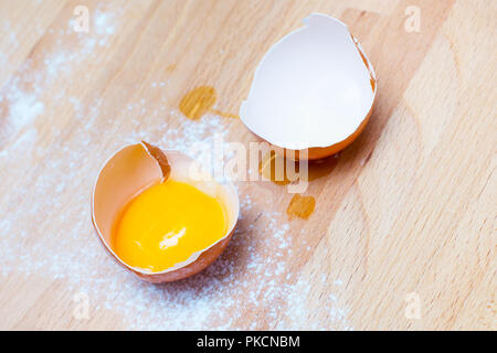 Cooking or baking background with close up broken egg, yolk in eggshell, flour on a wooden background Stock Photo