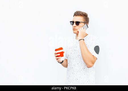 Stylish young man holding a cup of coffee in hand and talking on the phone. Stock Photo