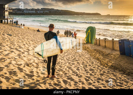 A surfer looking out over Fistral Beach in Newquay Cornwall during an intense sunset. Stock Photo