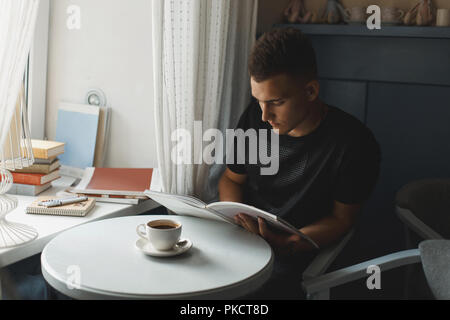 Handsome young man reading a book. Coffee on the table. Stock Photo