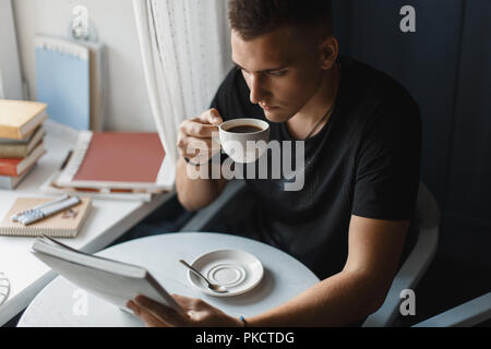 Young man reading a book and drinking coffee in a restaurant Stock Photo