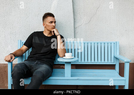 Handsome lonely man sits alone on a bench and drink coffee Stock Photo