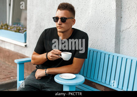 Handsome young man with coffee sitting on a bench. Stock Photo