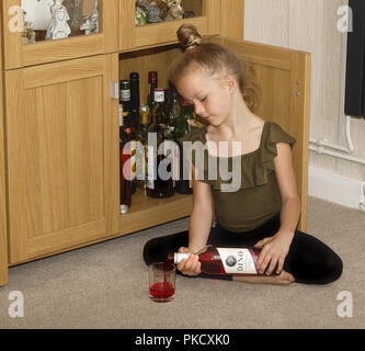 A six year old girl helping herself to wine from a drinks cabinet Stock Photo