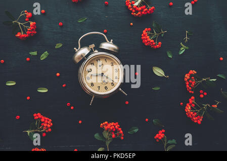 Flat lay vintage alarm clock on dark black background, top view minimal composition with retro floral arrangement Stock Photo