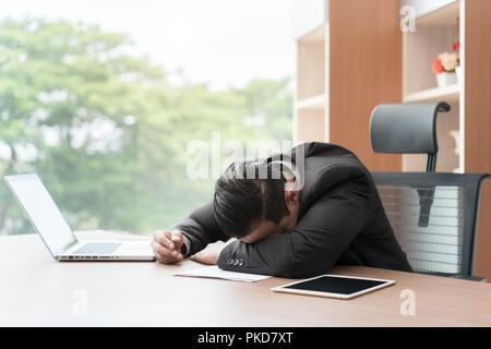 Tired overworked businessman sleeping over a laptop in a desk at job in his office. Asian businessman. Stock Photo