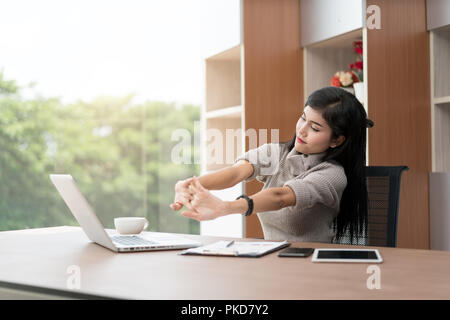 Young Asian businesswoman is relaxing in office. Asian businesswoman is stretching her body. Stock Photo