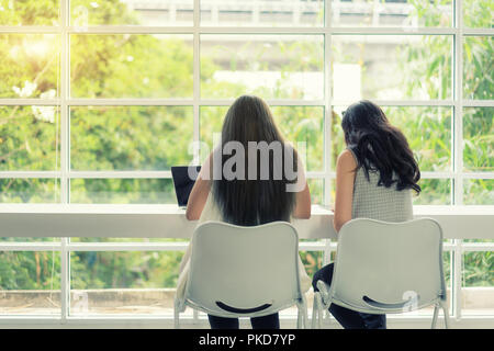Two Asian young business people gathered together at a table discussing an interesting idea in the cafe. Stock Photo