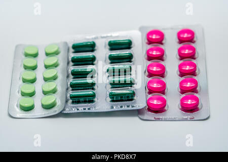 Pink tablets and green capsule and green tablets in blister pack on white background. Painkiller medicine. Pharmaceutical industry. Pharmacy drugstore Stock Photo