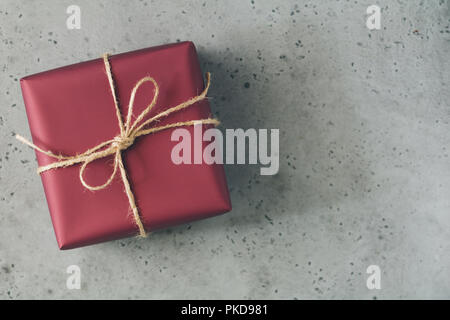 Gift box in a red wrapping paper is tied twine over a concrete grey background with copy space. Flat lay, top view. Stock Photo