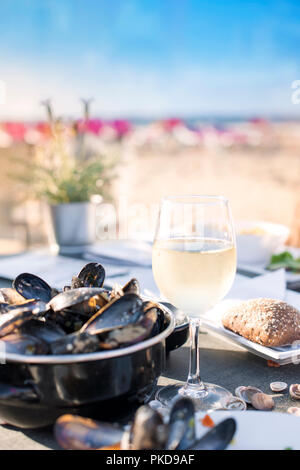 Mussels in a saucepan and a glass of cold white wine. Delicious seafood dinner in a restaurant on the beach. Copy space Stock Photo