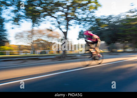 A blurred cyclist riding at high speed in warm morning sunlight in Centennial Park, Sydney Australia Stock Photo
