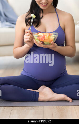 Cheerful pregnant woman eating fruit salad Stock Photo