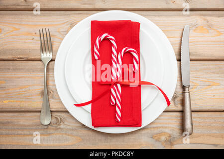 Christmas table setting. Candy canes on white plates and cutlery, wooden background, top view Stock Photo