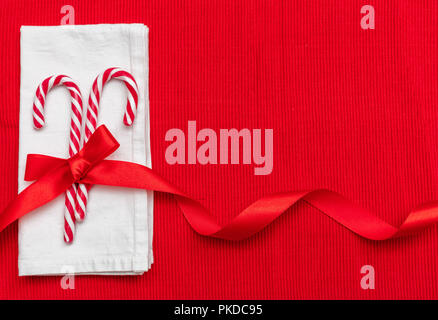 Christmas table setting. Candy canes with a red satin ribbon and a white napkin on red tablecloth, copy space Stock Photo
