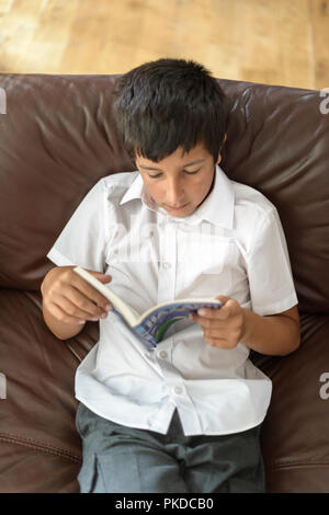 Surrey,UK-Young boy,10 years old  in school uniform  reading  at home-elevated view