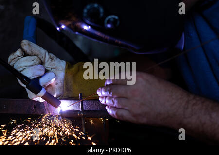 A man with protective helmet welding two pieces of metal. Sparks flying. Stock Photo