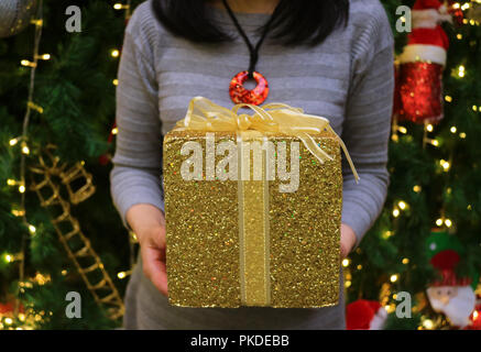 Season of giving! A woman holding gold glitter square shape gift box in her hands Stock Photo