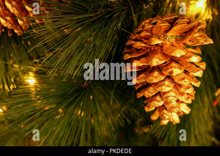 Shiny gold colored dry pine cone ornament hanging on sparkling Christmas tree Stock Photo