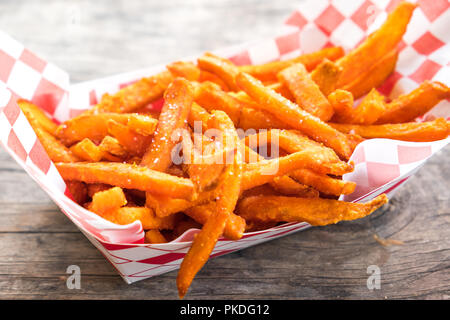 Paper basket of sweet potato fries with salt on rustic wooden table Stock Photo