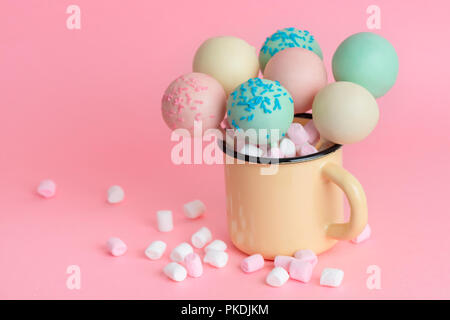 pink, blue, white icing pop cakes and marshmallows in cup over pink background Stock Photo