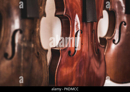 Macro shot of beautiful, handmade wooden violins, hanging on white background with shallow depth of field. A result of expert carpenters and luthiers. Stock Photo