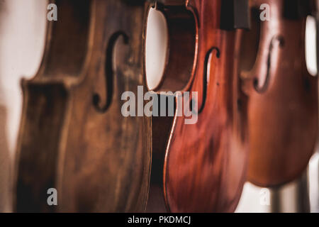 Macro shot of beautiful, handmade wooden violins, hanging on white background with shallow depth of field. A result of expert carpenters and luthiers. Stock Photo
