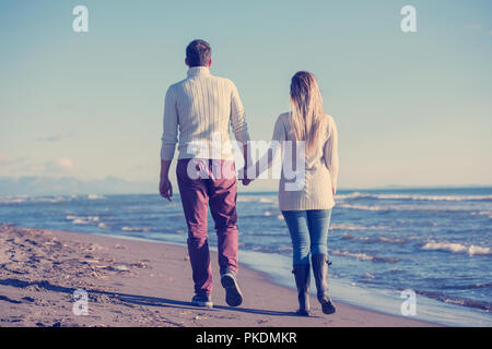 Young couple having fun walking and hugging on beach during autumn sunny day Stock Photo