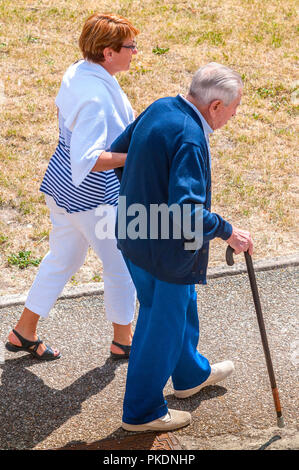 Woman helping man with walking stick along pavement - France. Stock Photo