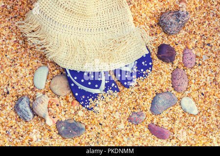 Beach scene. Sun straw hat and flip-flop sandals lying on sea coquina shells on the beach Stock Photo