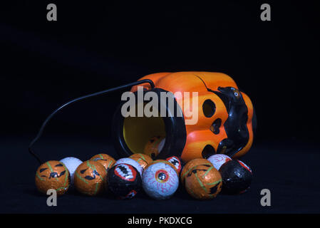 Pumpkin shaped halloween lantern with black cat coming out With lots of round chocolate sweets enclosed in a funny face, on a black background. Useful Stock Photo