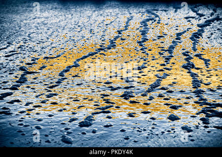 Receding wave ripples at low tide with bubbles and reflections of sunset and sky.