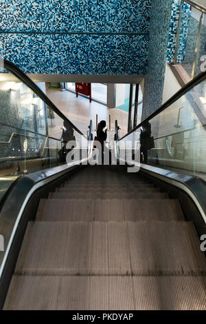 Silhouette of girl climbing airport escalators with suitcase. Stock Photo