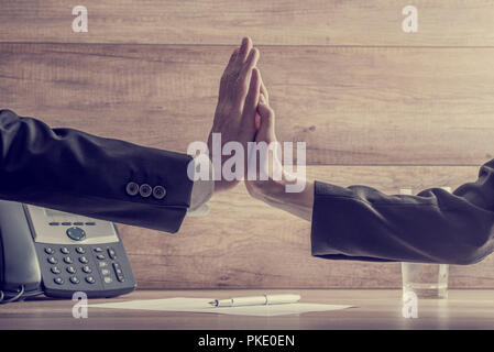Retro image of business colleagues making high five gesture over a contract or document with a pen lying on it. Conceptual of agreement and cooperatio Stock Photo