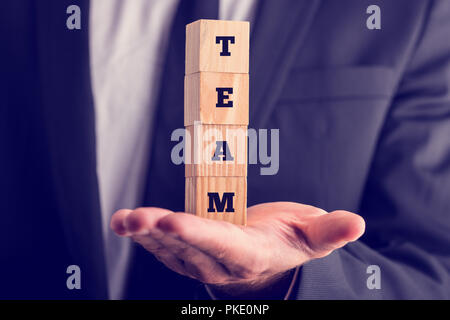 Retro style image of a  business man holding wooden cubes reading - Team - stacked on the palm of his hand acknowledging the power of cooperation and  Stock Photo