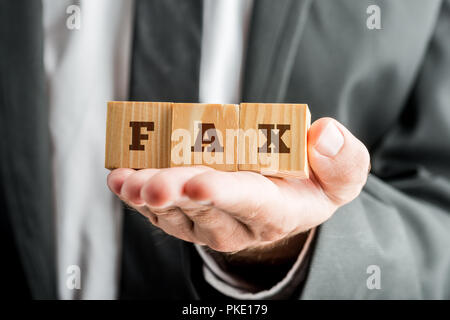 Front closeup view of businessman hand holding three wooden cubes reading FAX. Stock Photo