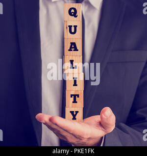 Close Up of Businessman Holding Stacked Letter Blocks Spelling Quality in Hand. Stock Photo