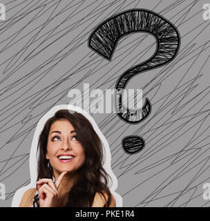 Thinking smiling positive woman looking up on one big creative question marks above the head on grey background. Closeup portiat with sketch illustrat Stock Photo