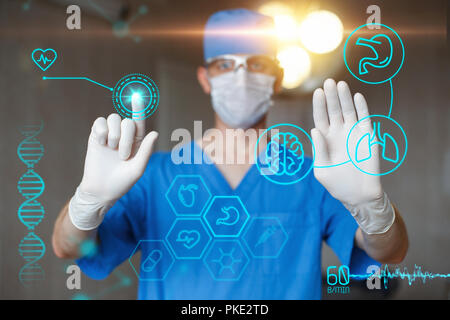 Doctor in blue uniform touch display with infographics. Modern professional surgeon in the operating room. Medical icons on the desktop. Stock Photo