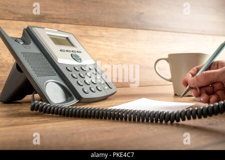Closeup of male hand taking important notes as he answers a call on a classical landline telephone. Concept of assistance and secretary work. Stock Photo