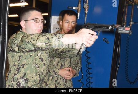 LAKES, Ill. (July 24, 2018) Gunner’s Mate 1st Class Thuan Vo, an instructor at the USS Missouri Small Arms Marksmanship Trainer (SAMT) at Recruit Training Command (RTC), observes University of Illinois Naval ROTC midshipman candidate Hunter Deal, from Freeport, Ill., as he operates a simulated M9 Beretta 9mm pistol. SAMT uses red laser lights and pneumatic air to simulate the firing and hits on a computer target.  More than 65 young men and women entering their freshman year of the NROTC program participated in a two-week pilot program designed to provide standardized entry-level militarizatio Stock Photo