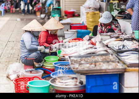 Women cleaning freshly caught fish and other seafood for sale. Local delicacies displayed on a counter at a vintage Asian market of Ben Thanh. Stock Photo