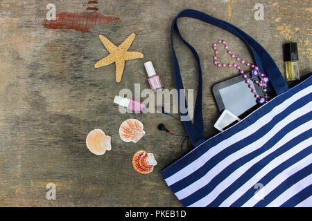Beach bag, cosmetics and women's accessories on old wooden background. Top view. Stock Photo
