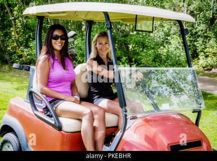 Two beautiful female golfers posing for a picture while sitting in a golf cart on the golf course during a golf tournament; Edmonton, Alberta, Canada Stock Photo