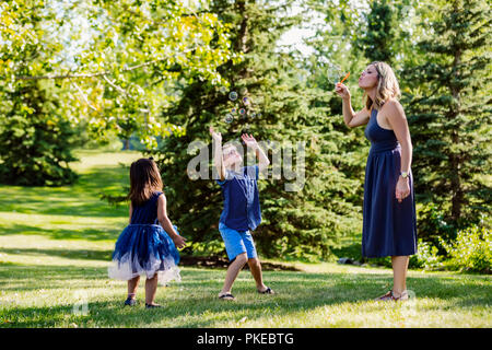 A mother blowing bubbles for her kids while on a family outing in a park on a warm fall day; Edmonton, Alberta, Canada Stock Photo