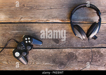 Video game controller and headphones on old wooden background. Top view. Stock Photo
