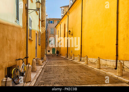Man and dog walking down a street between yellow buildings; Saint-Tropez, France Stock Photo