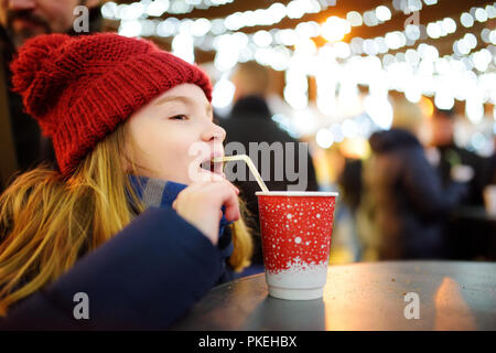 Cute little girl drinking hot chocolate on traditional Christmas market. Child enjoying sweets, candies and gingerbread on magical Xmas time.