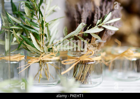 Fresh olive branches and dried lavender in square glass vases on a wooden table at home Stock Photo